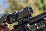 Close-up of a rifle with a scope against a blurred natural background
