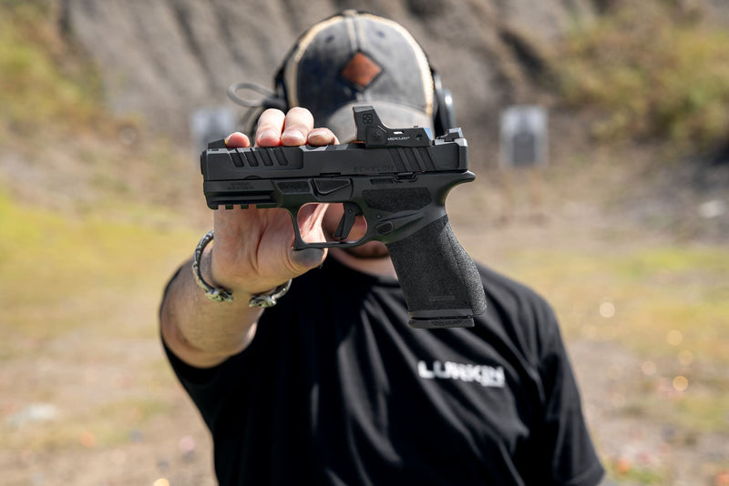 Person holding a handgun with a blurred background. MERCURY Reflex Sight in outdoor range environment mounted and ready
